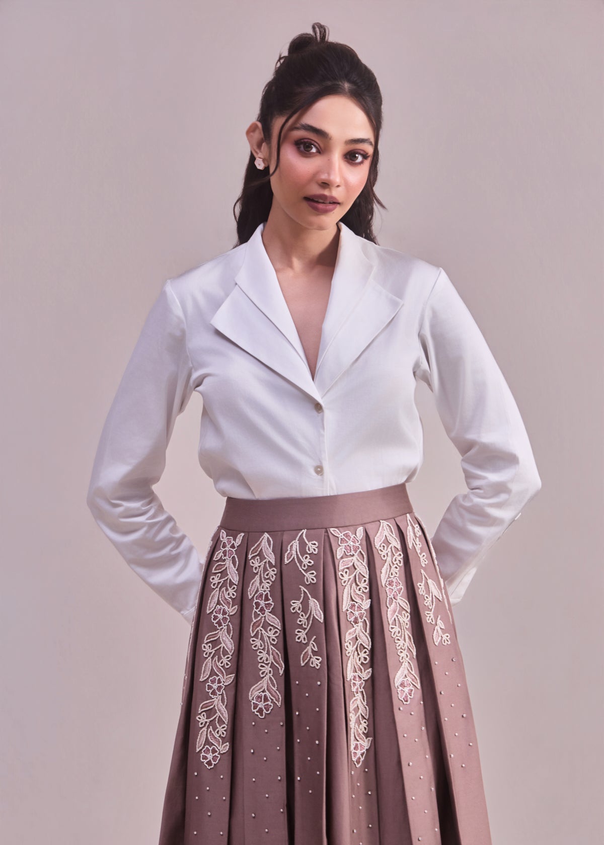 Woman wearing a white top and brown skirt with lace details on a plain background