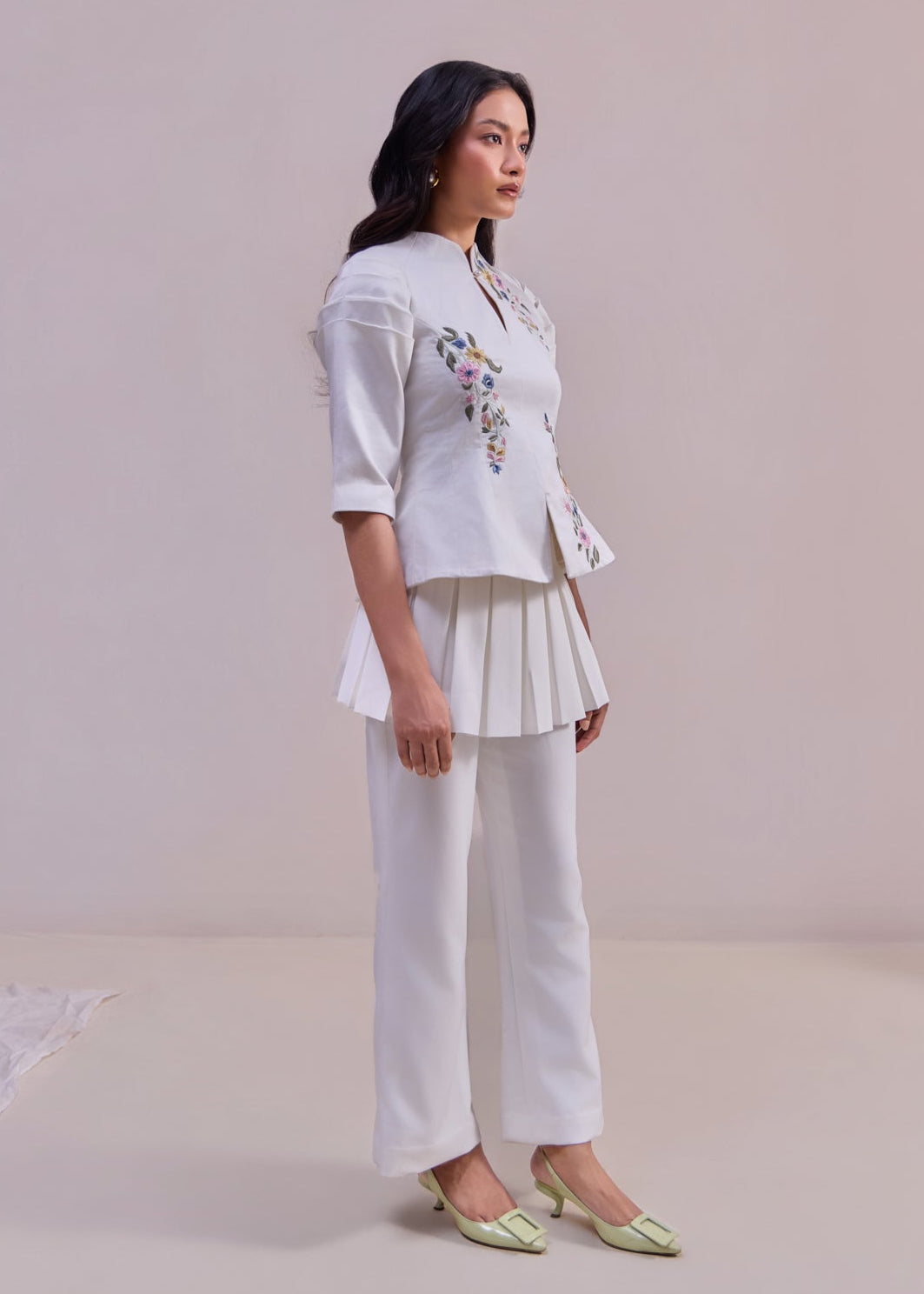 Woman wearing a white outfit with floral embroidery on a plain background