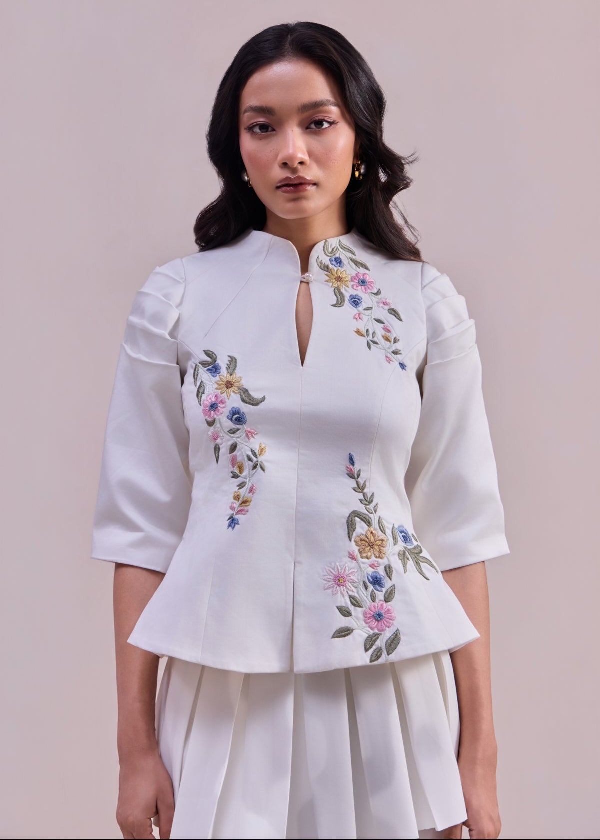 Woman wearing a white blouse with floral embroidery on a plain background