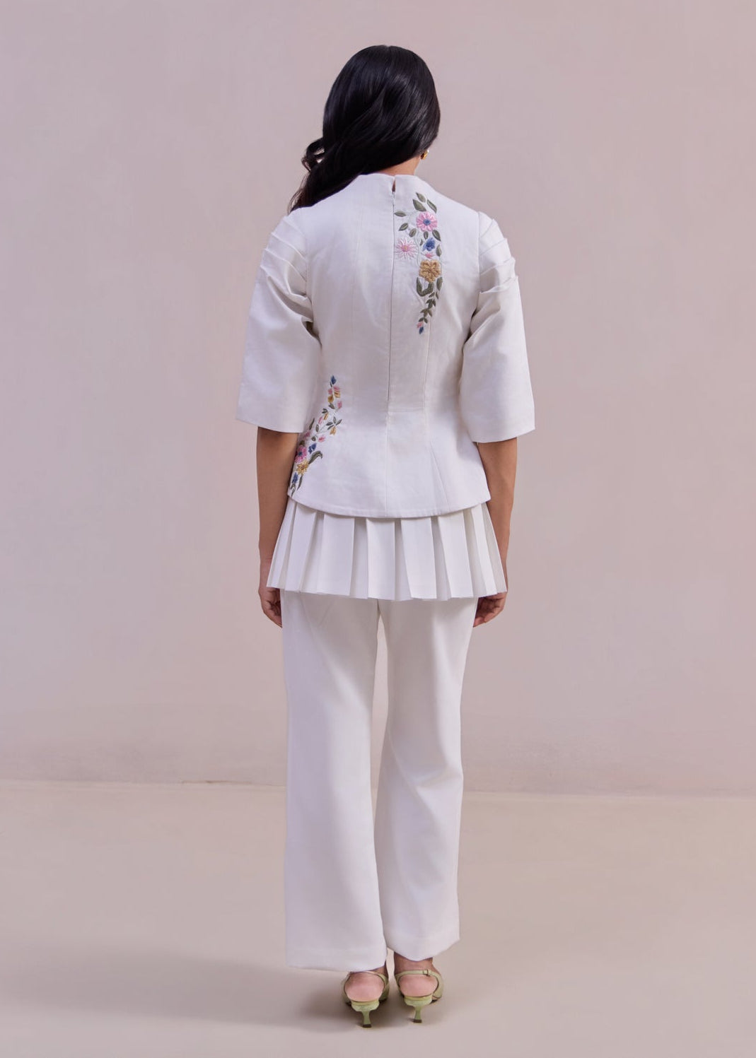 Person wearing a white outfit with floral embroidery on a plain background