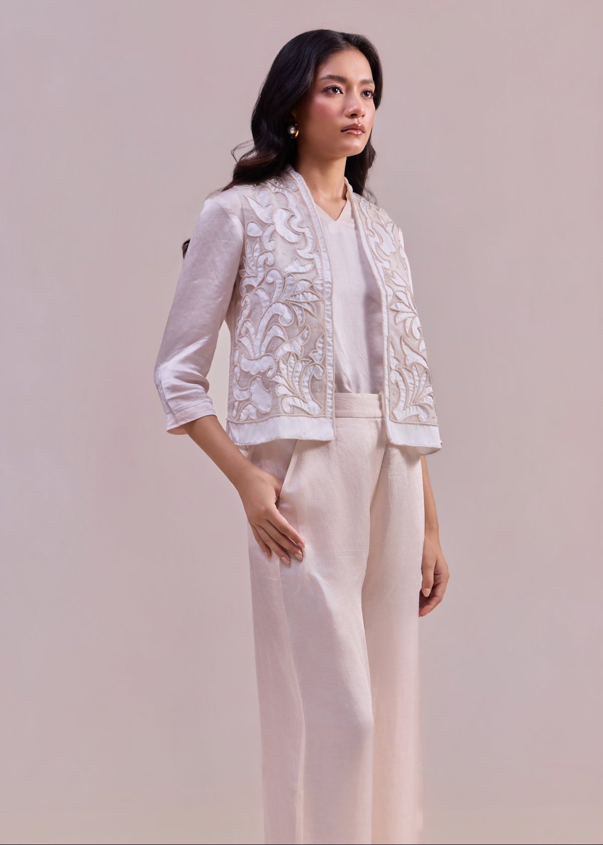 Woman wearing a white embroidered jacket and pants on a plain background