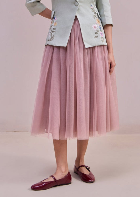 Woman wearing a light green blazer with floral embroidery and a pink skirt against a plain background