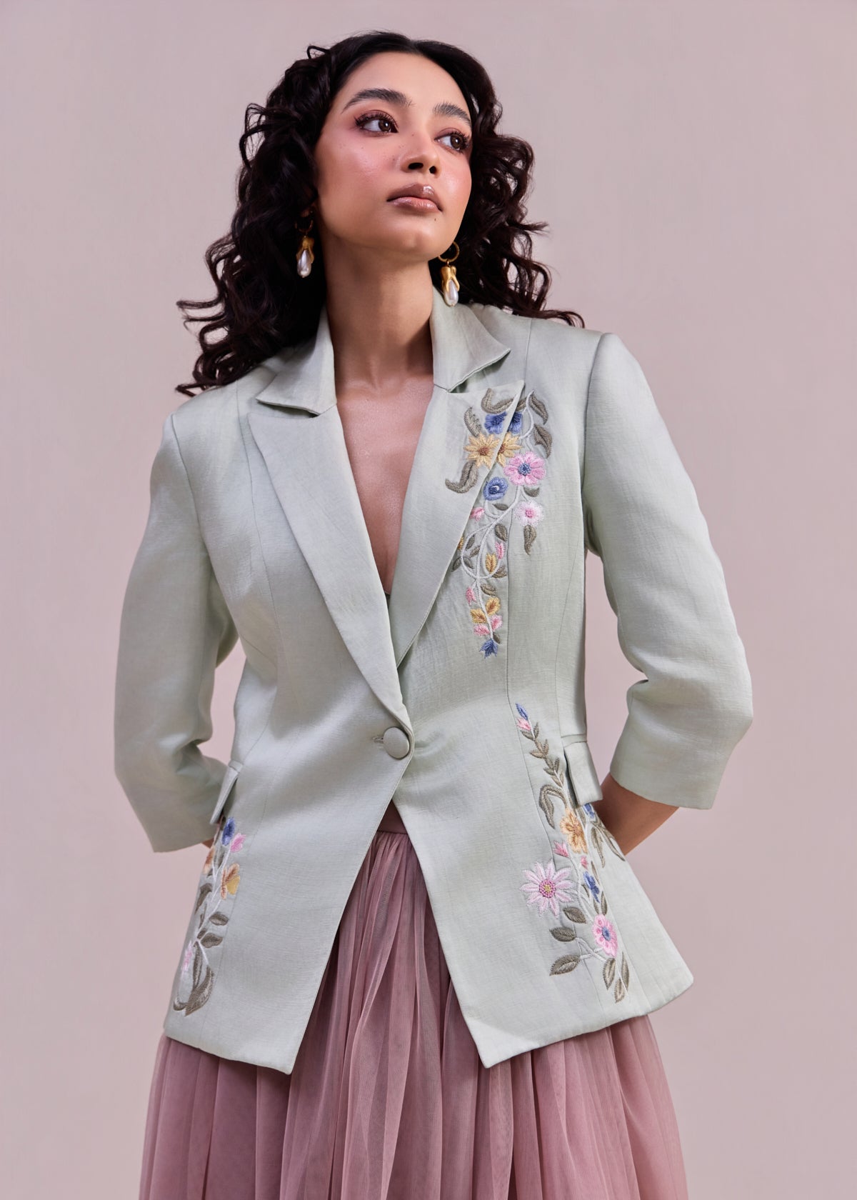 Woman wearing a light gray blazer with floral embroidery on a pink background