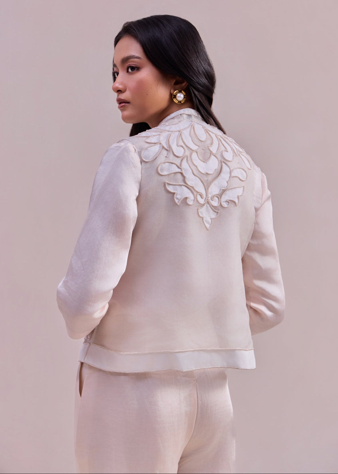 Woman wearing a white embroidered jacket on a beige background