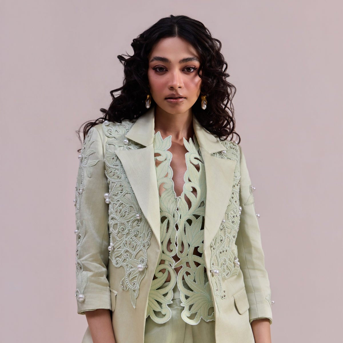 Woman wearing a light green suit with lace details on a plain background