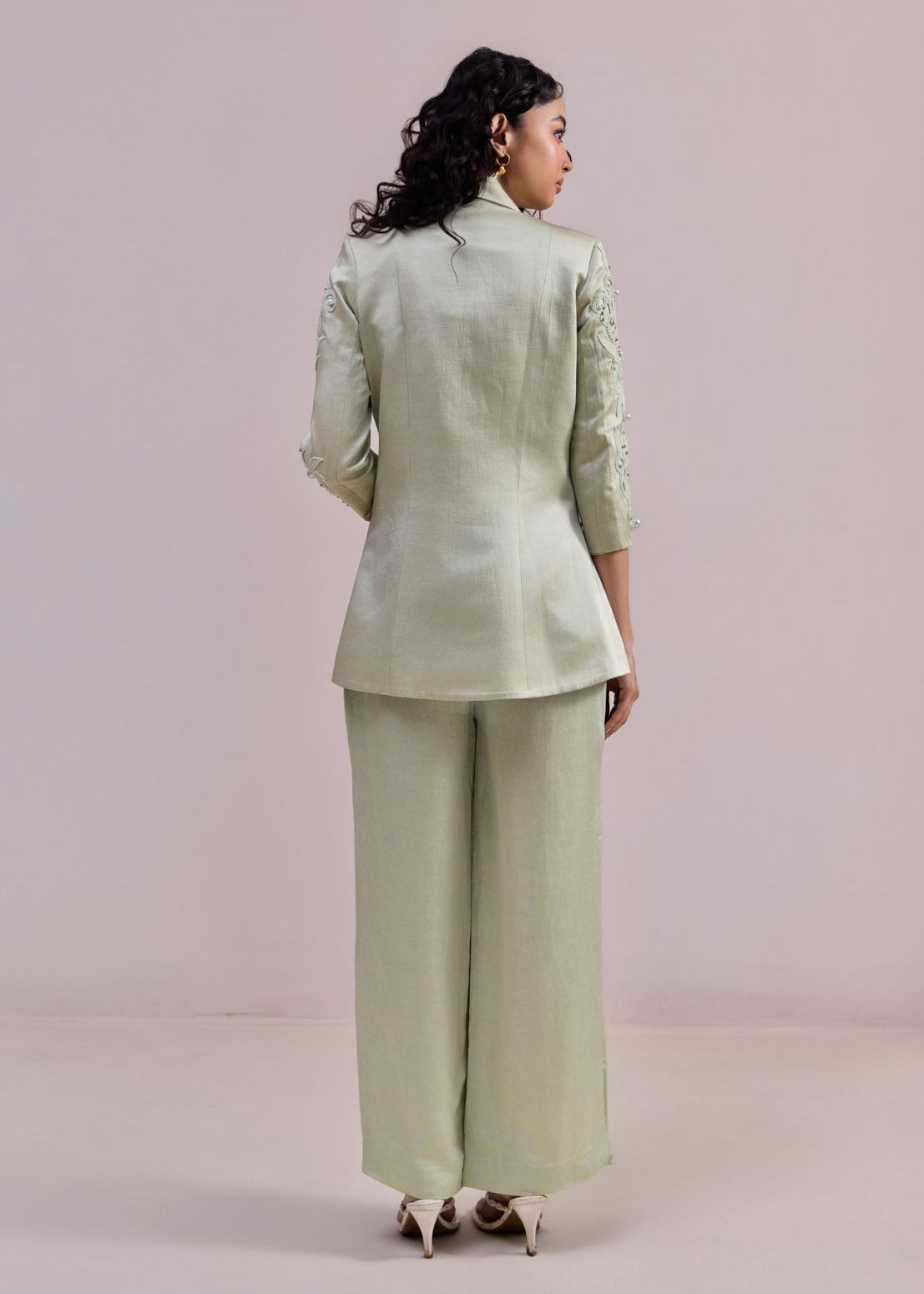 Woman wearing a light green suit standing against a plain background
