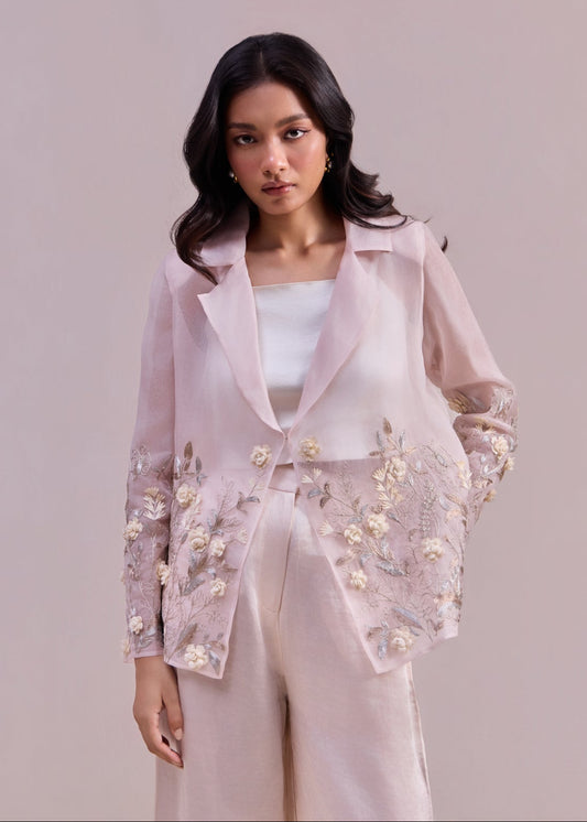 Woman wearing a light pink embroidered outfit against a plain background
