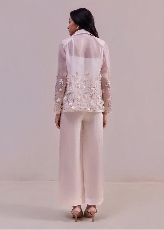 Woman wearing a light pink embroidered jacket and pants on a plain background