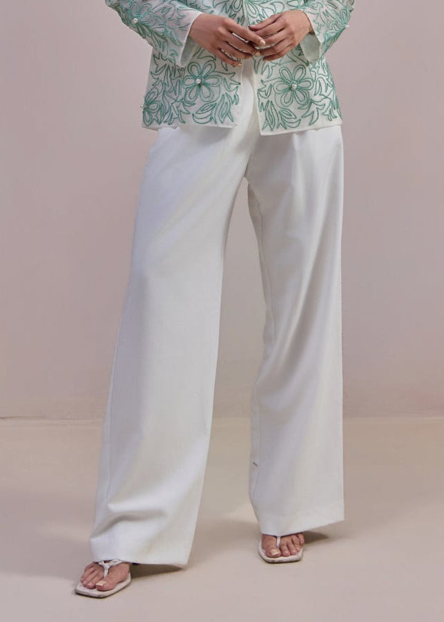 Woman wearing a green patterned blazer and white pants against a plain background