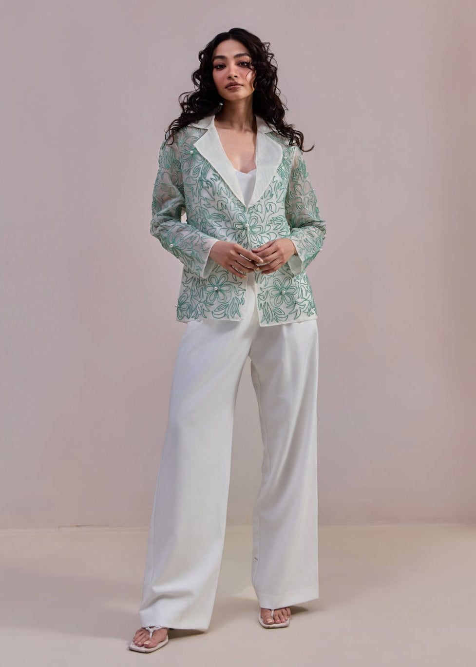 Woman wearing a green patterned blazer and white pants against a plain background