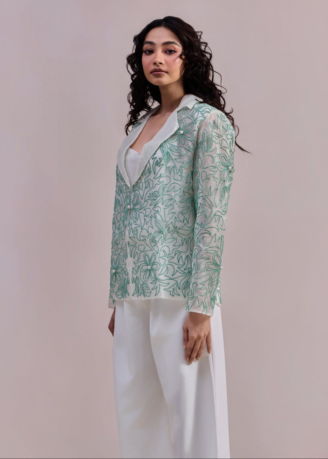 Woman wearing a green floral blouse and white pants against a plain background