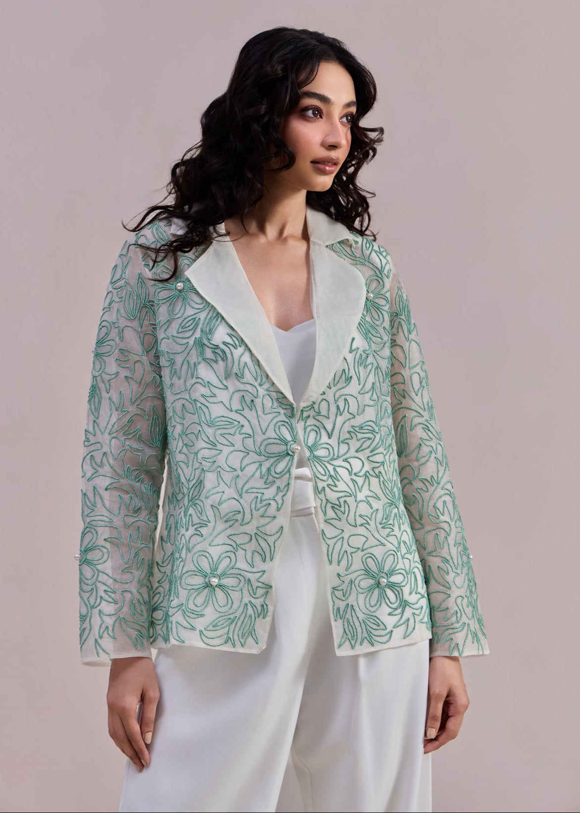 Woman wearing a light green floral blazer over a white top and pants on a beige background