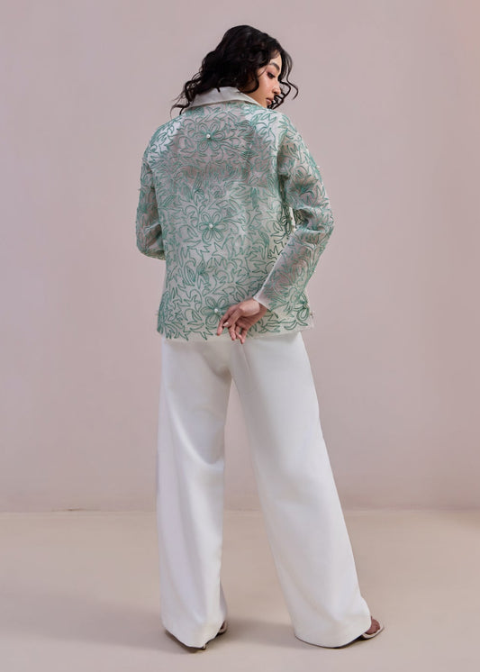 Woman wearing a green patterned top and white pants on a beige background