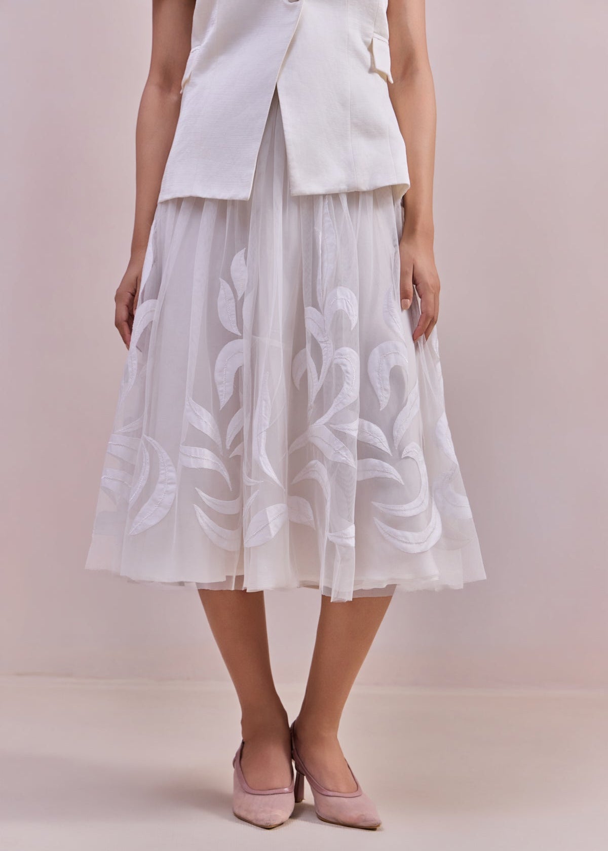 Woman wearing a white dress with floral embroidery on a plain background