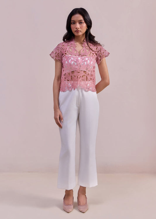 Woman wearing a pink lace top and white pants on a plain background
