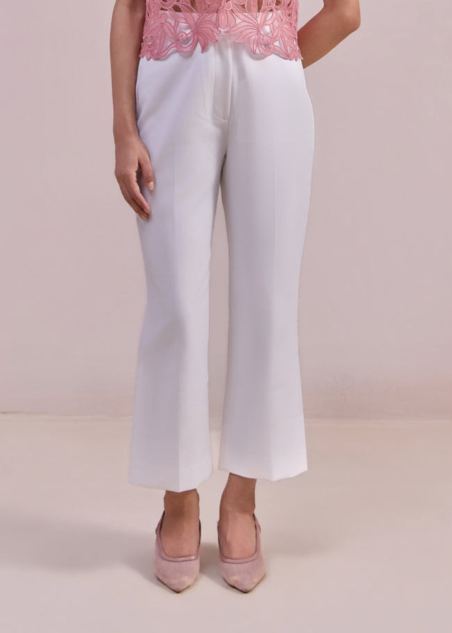 Woman wearing a pink lace top and white pants on a plain background