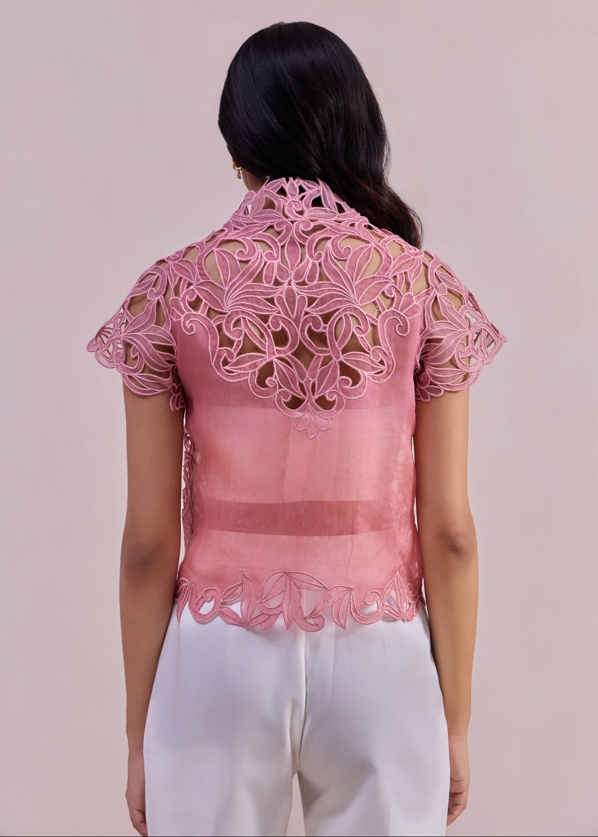 Woman wearing a pink lace top with a plain background