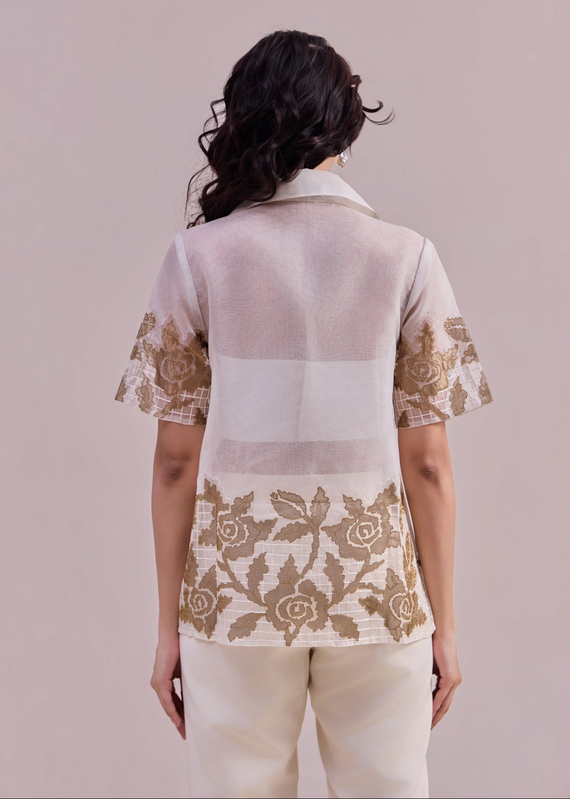Woman wearing a light-colored blouse with floral lace details on a plain background