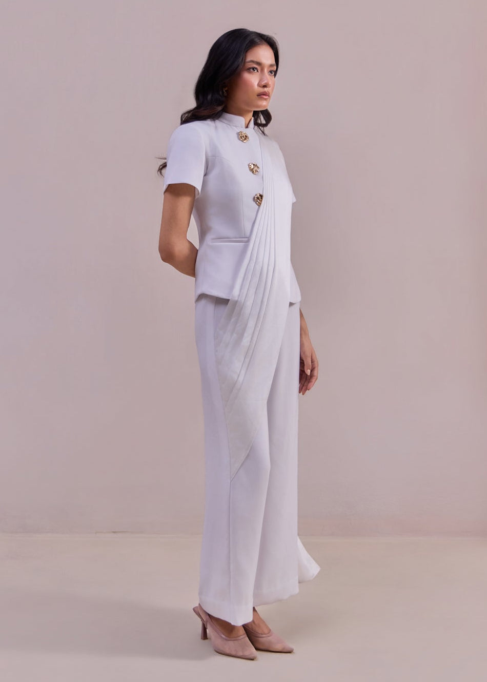 Woman wearing a white saree with a matching blouse against a plain background