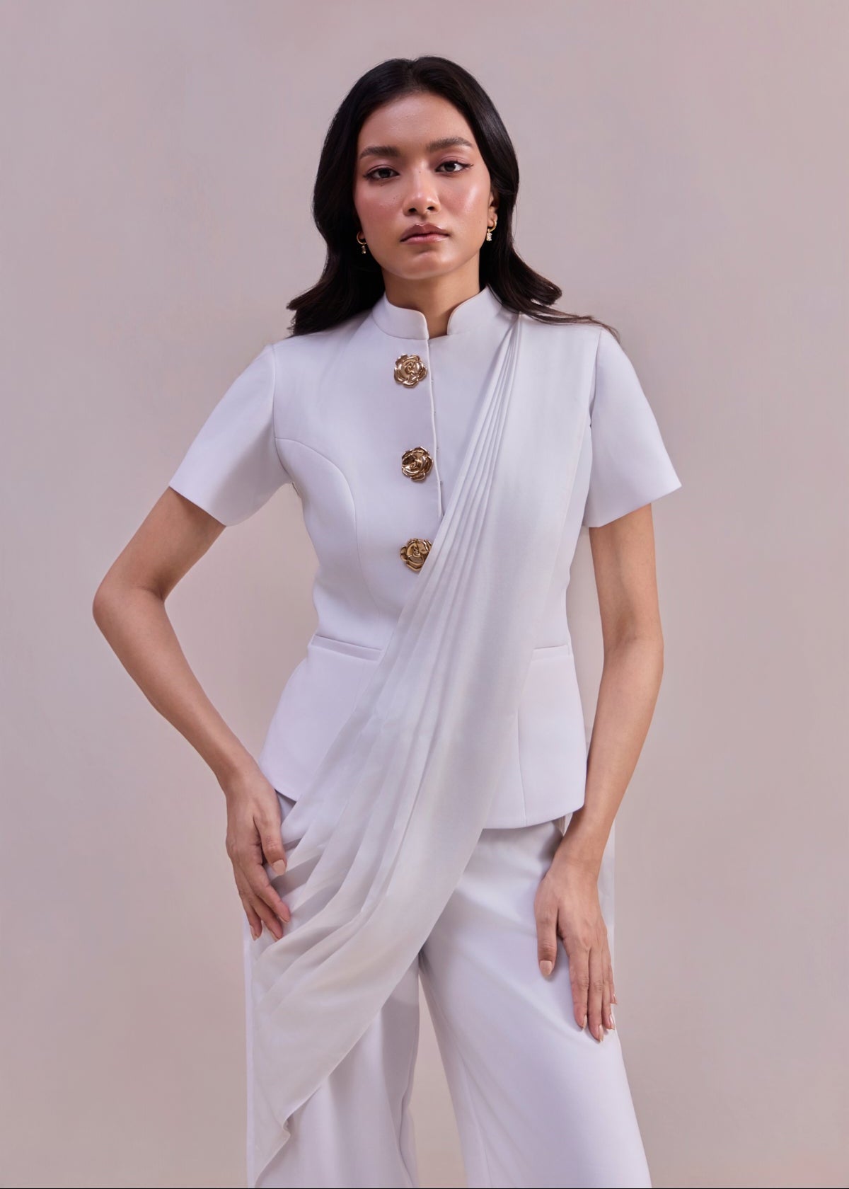 Woman wearing a white saree with gold accents against a plain background