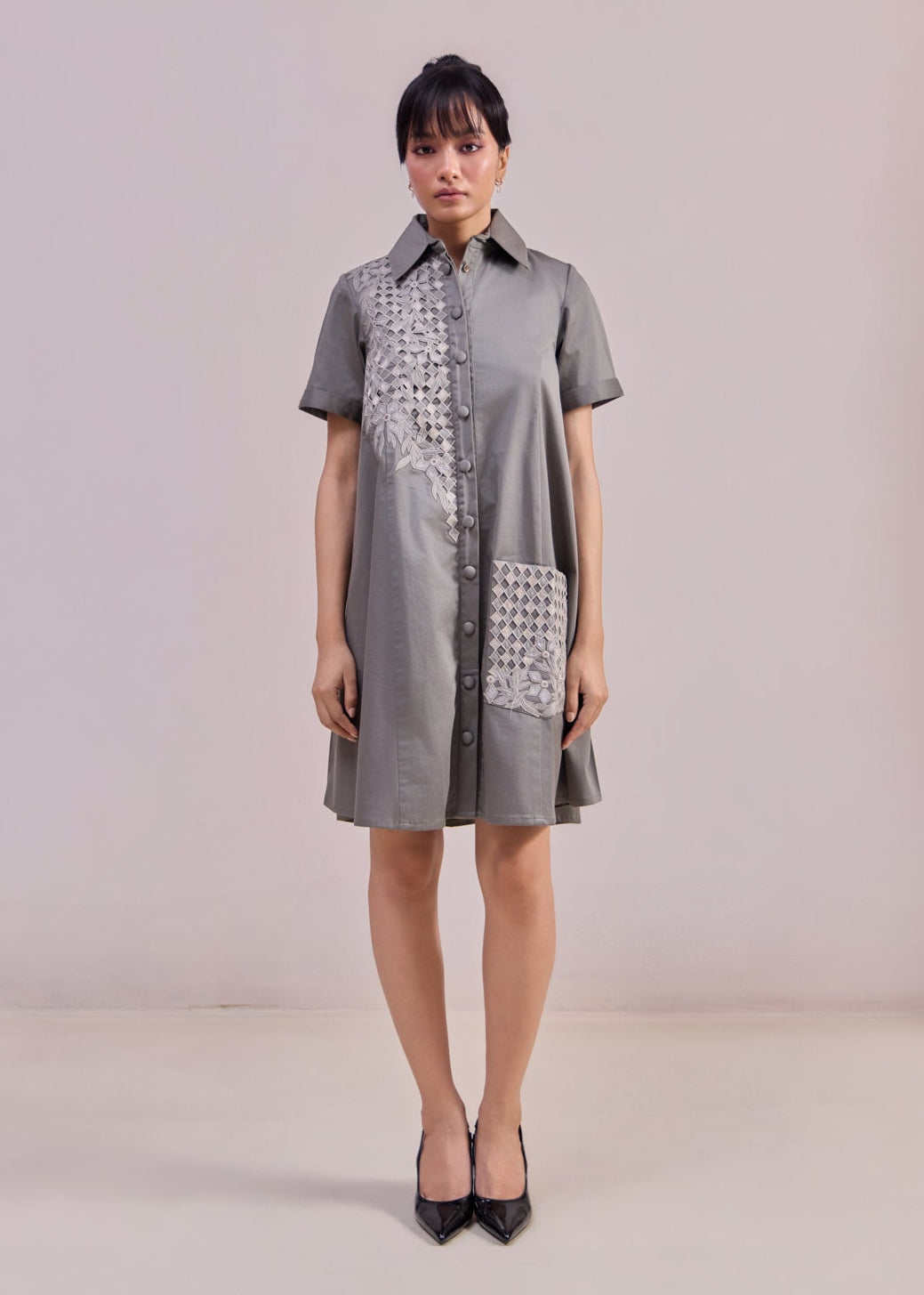 Woman wearing a gray dress with patterned pockets against a plain background
