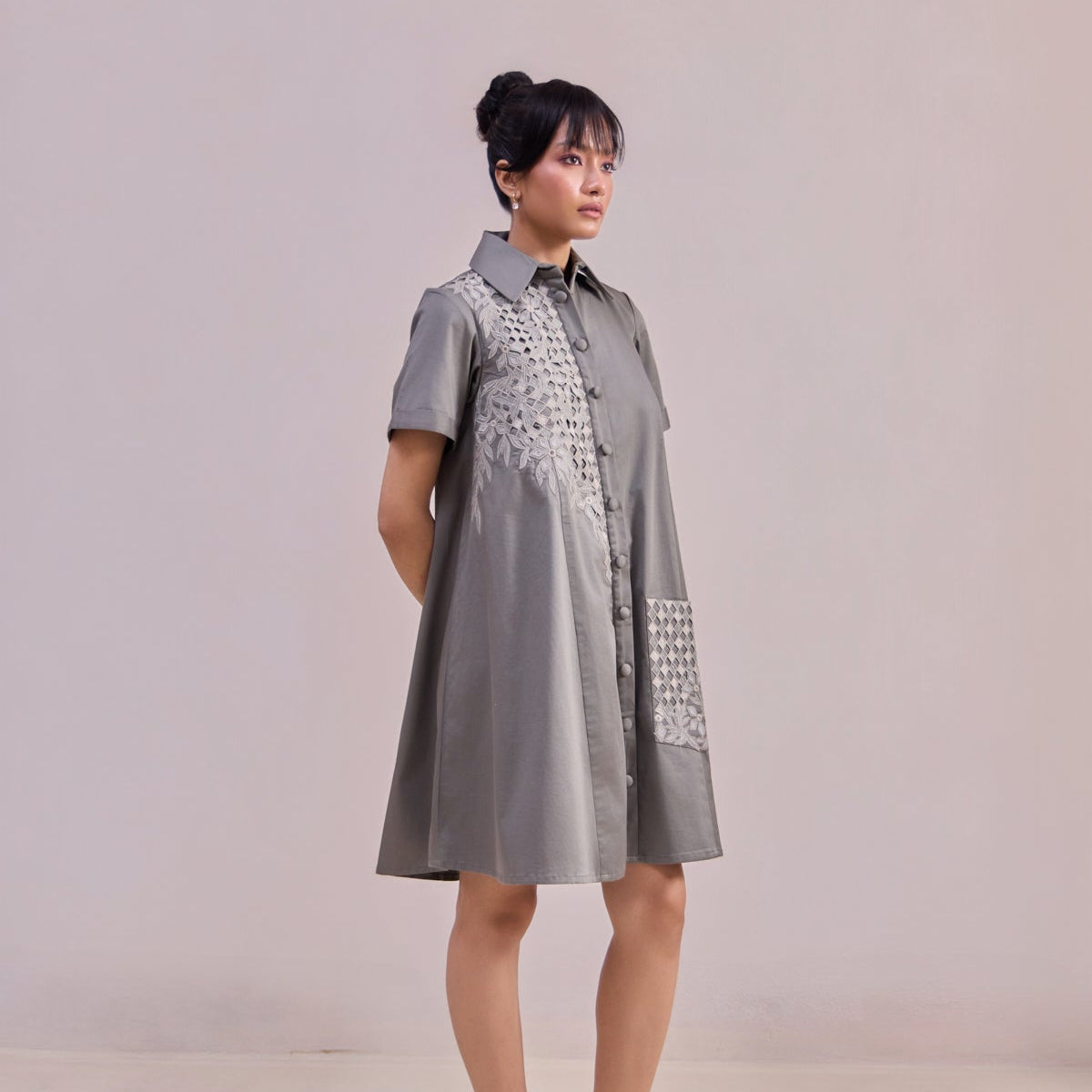 Woman wearing a gray dress with decorative patterns on a plain background