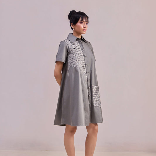 Woman wearing a gray dress with decorative patterns on a plain background