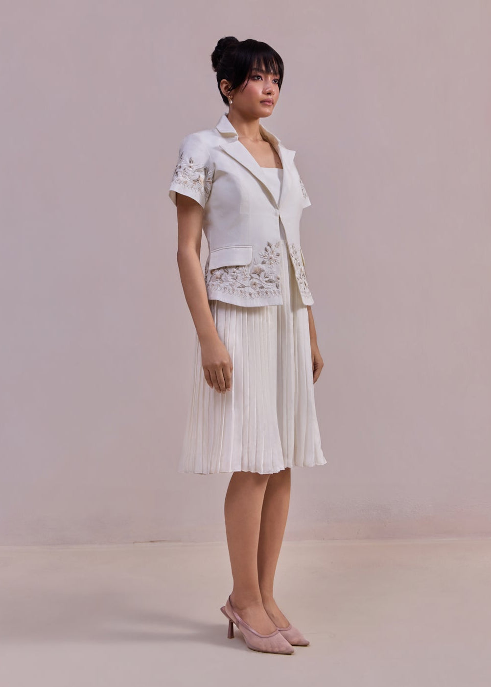 Woman wearing a white outfit with lace details against a plain background