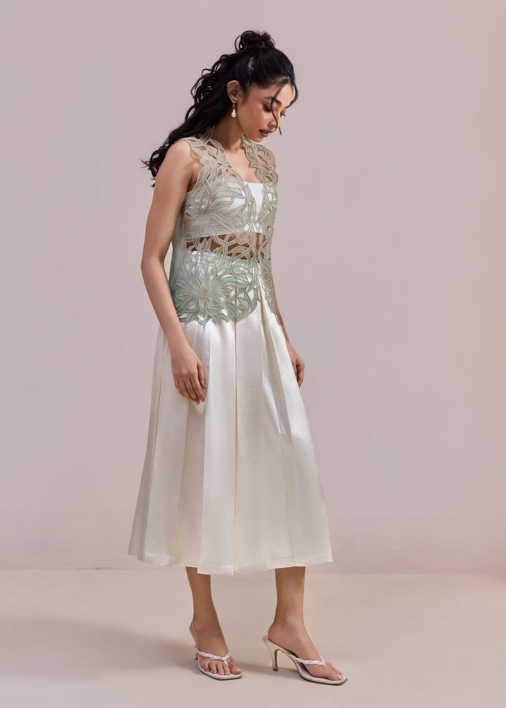 Woman wearing a light green sequined top and white skirt against a plain background