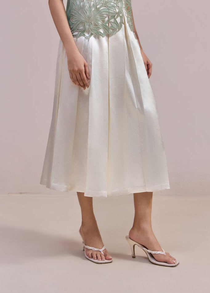 Woman wearing a light green sequined top and white skirt against a plain background