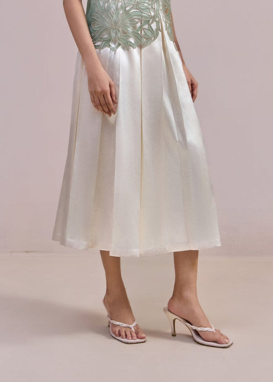 Woman wearing a light green sequined top and white skirt against a plain background
