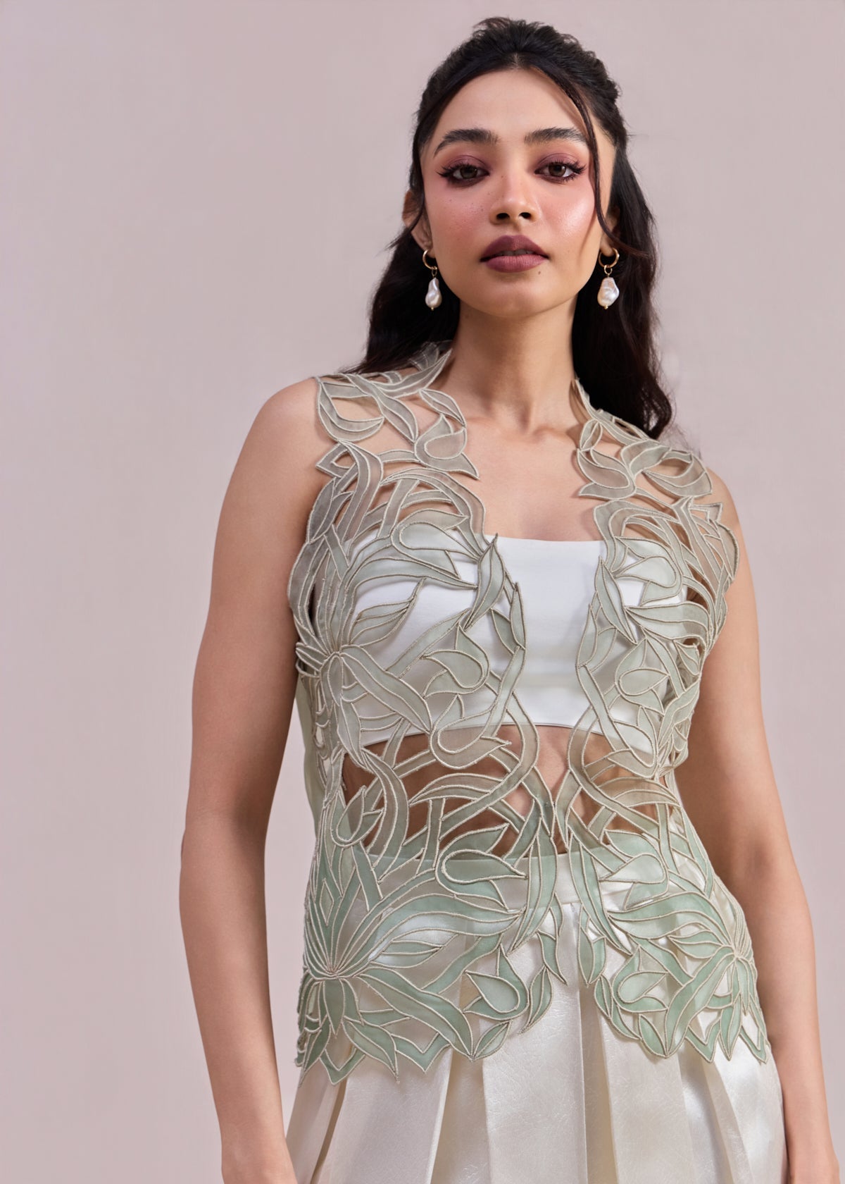 Woman wearing a light green embroidered top and white skirt against a beige background