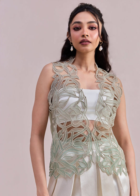 Woman wearing a light green embroidered top and white skirt against a beige background