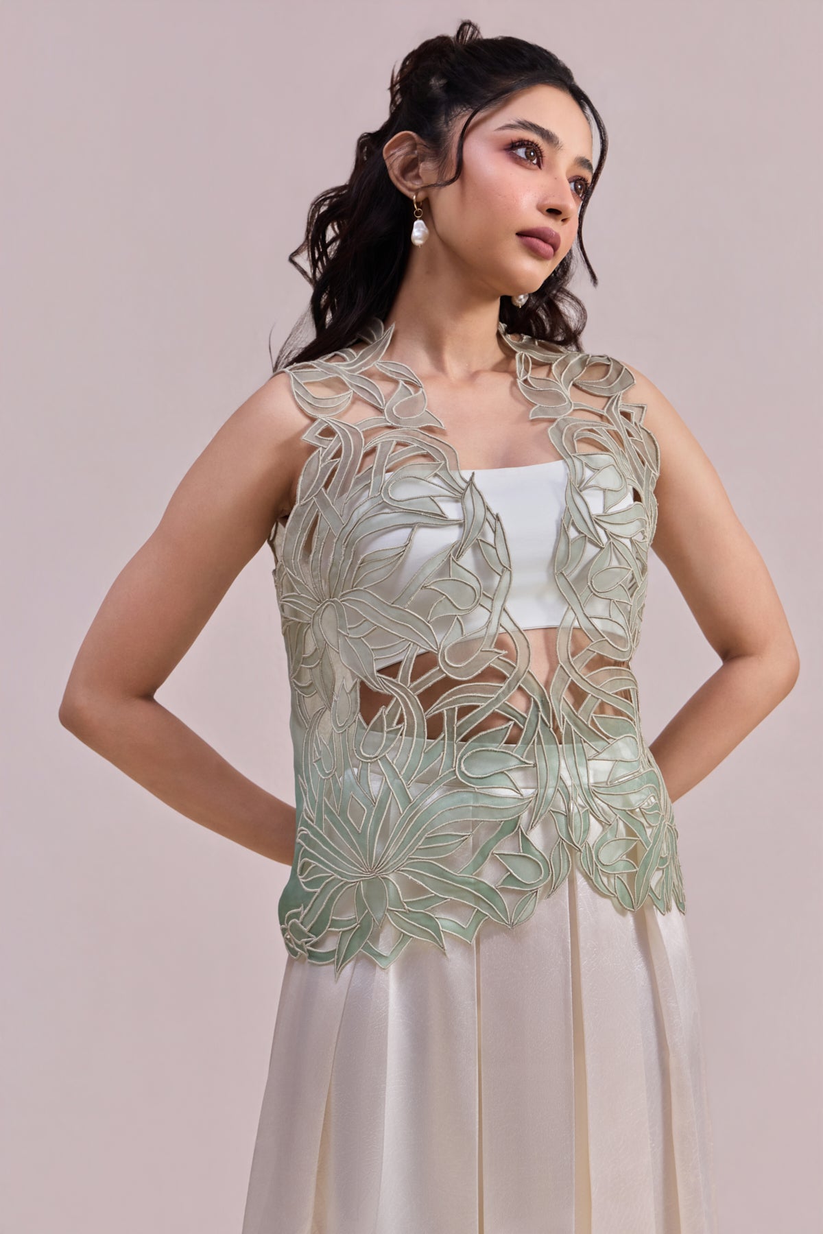 Woman wearing a light green floral lace top with a plain background