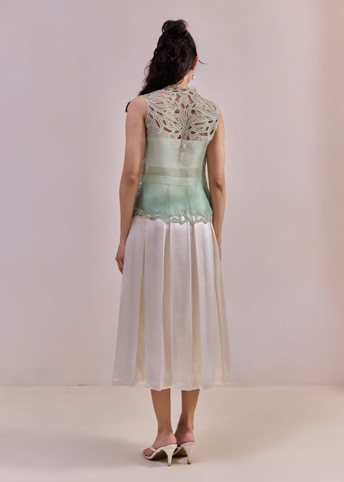 Woman wearing a light green sleeveless top with lace details and white pants on a plain background