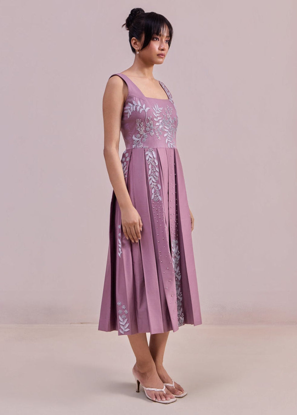 Woman wearing a purple dress with floral embroidery on a plain background