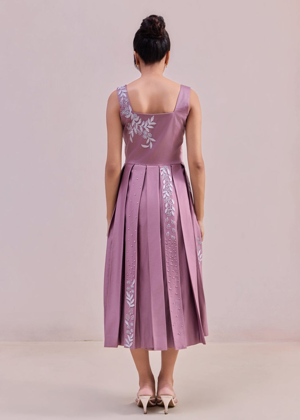 Woman wearing a purple dress with floral embroidery on a plain background