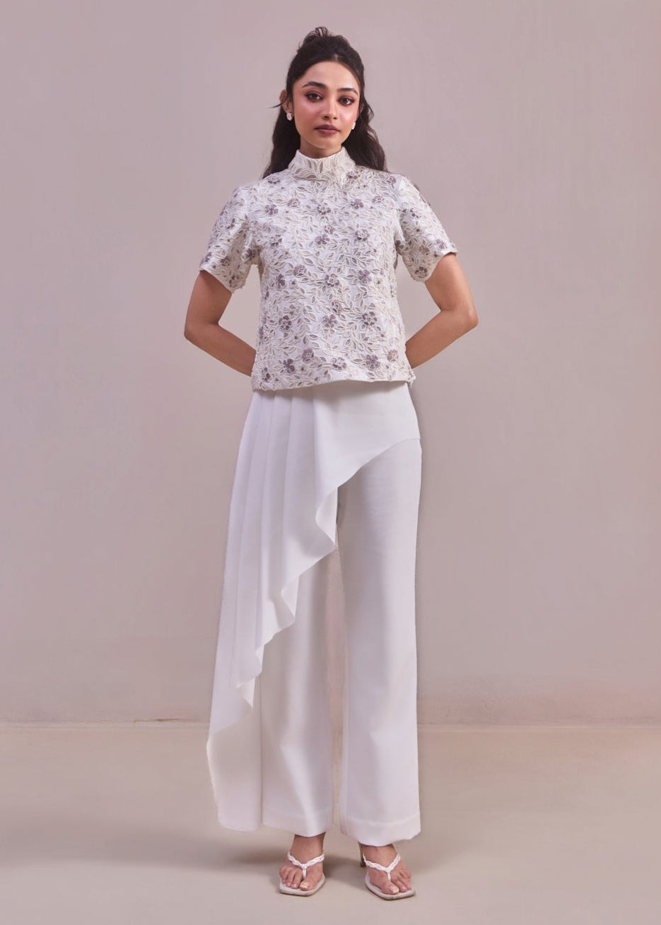 Woman wearing a floral top and white pants against a plain background