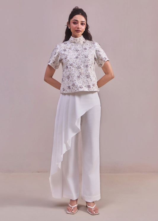 Woman wearing a floral top and white pants against a plain background