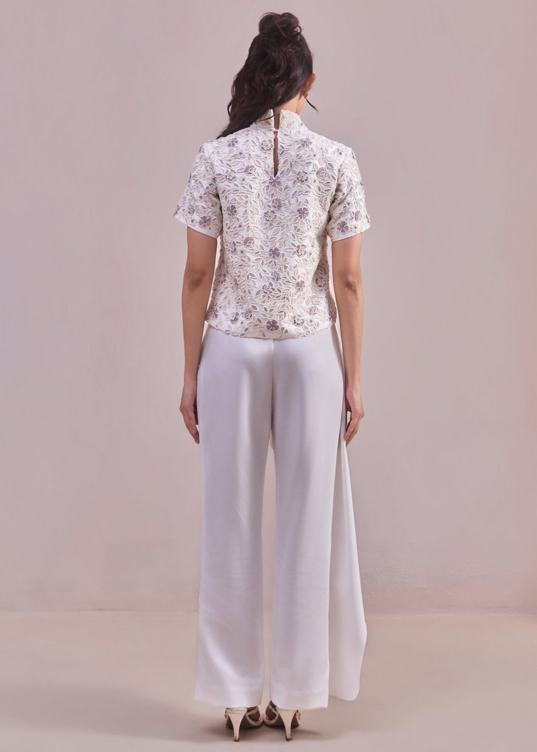 Person wearing a patterned top and white pants against a plain background