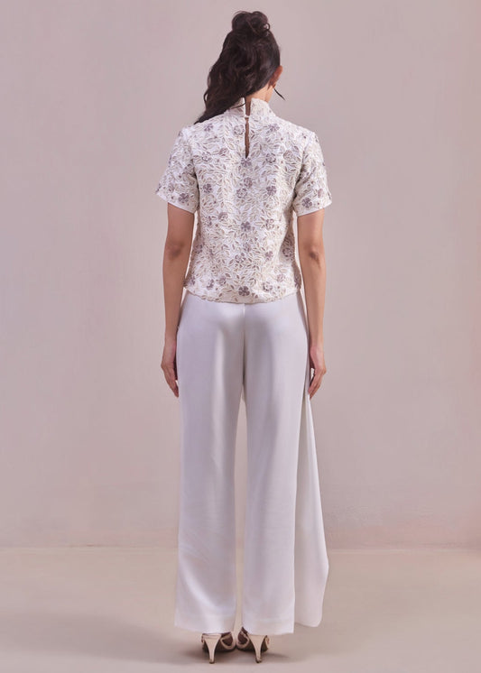 Person wearing a patterned top and white pants against a plain background