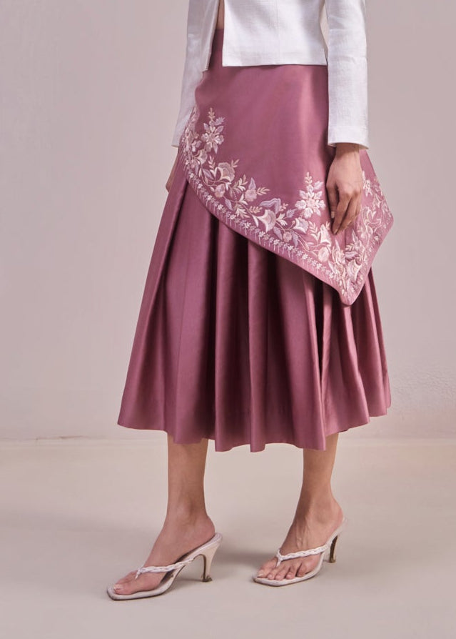 Woman wearing a white blouse and pink skirt with floral embroidery against a plain background