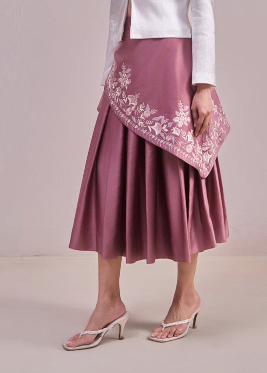 Woman wearing a white blouse and pink skirt with floral embroidery against a plain background
