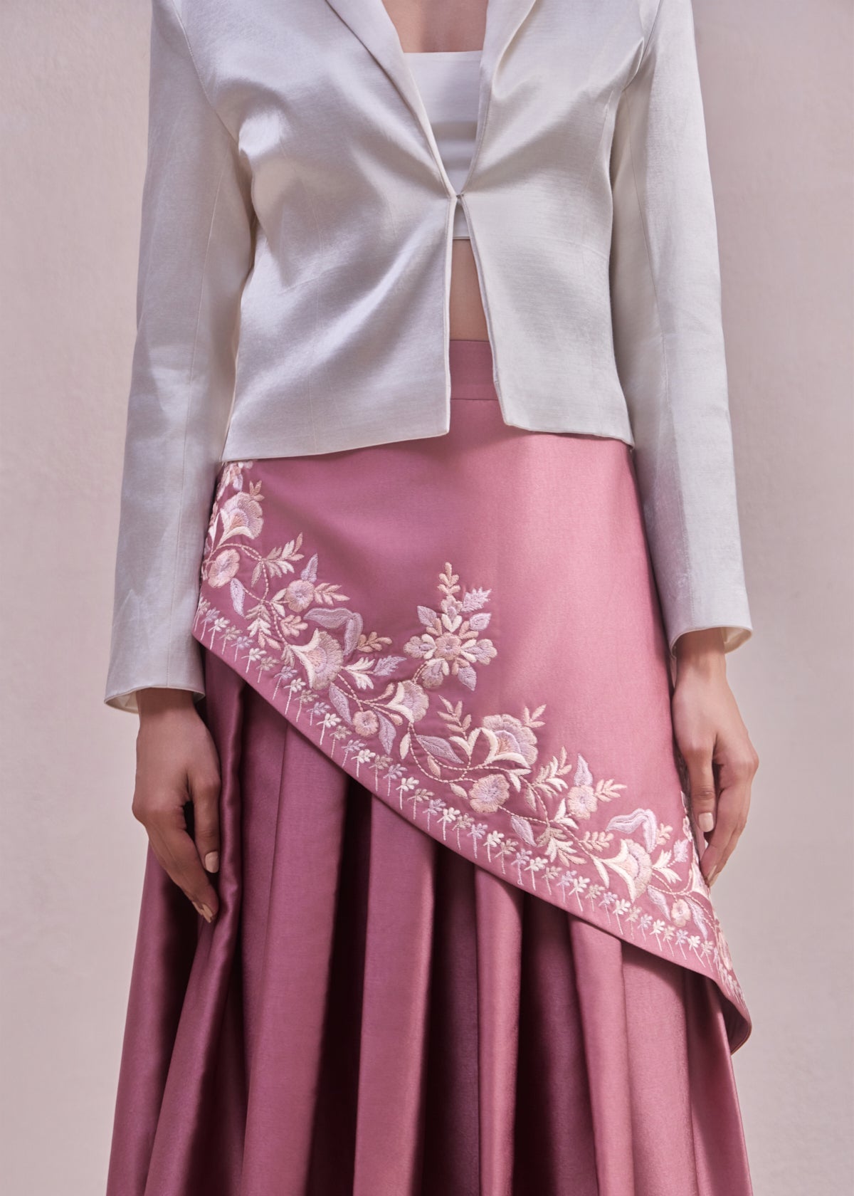 White jacket over a pink skirt with floral embroidery on a plain background