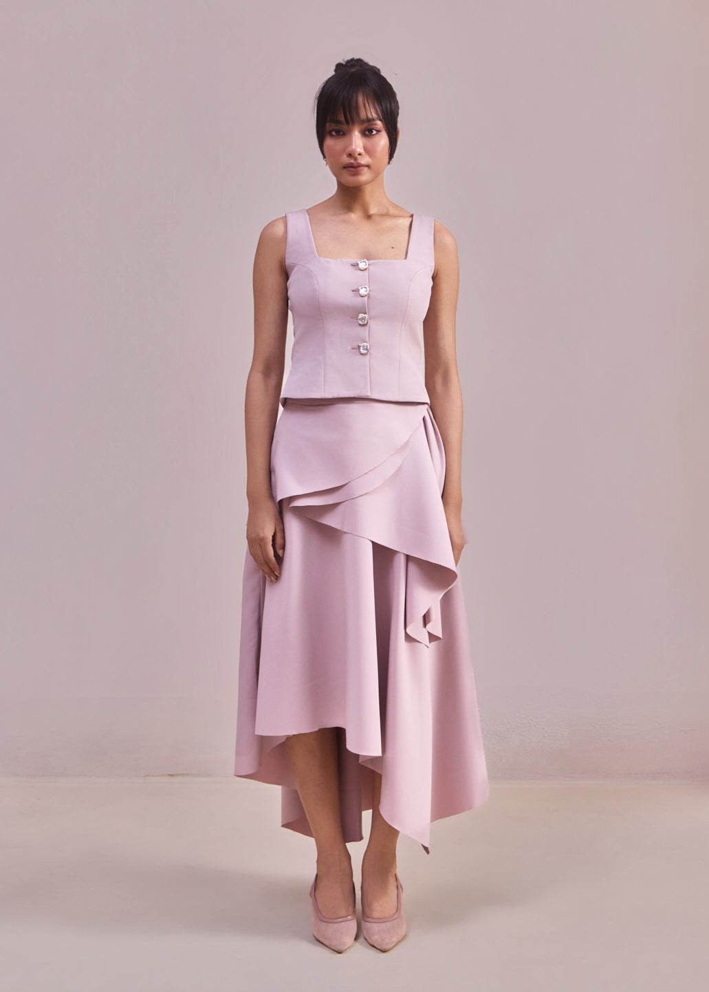 Woman wearing a light pink dress with a buttoned top and layered skirt on a plain background