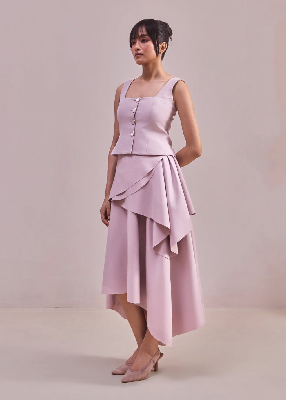 Woman wearing a light pink dress with a button-up top and layered skirt against a plain background