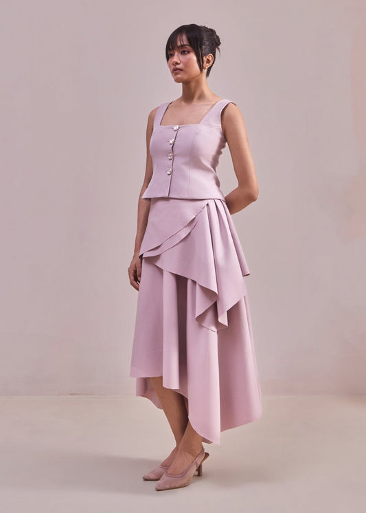 Woman wearing a light pink dress with a button-up top and layered skirt against a plain background