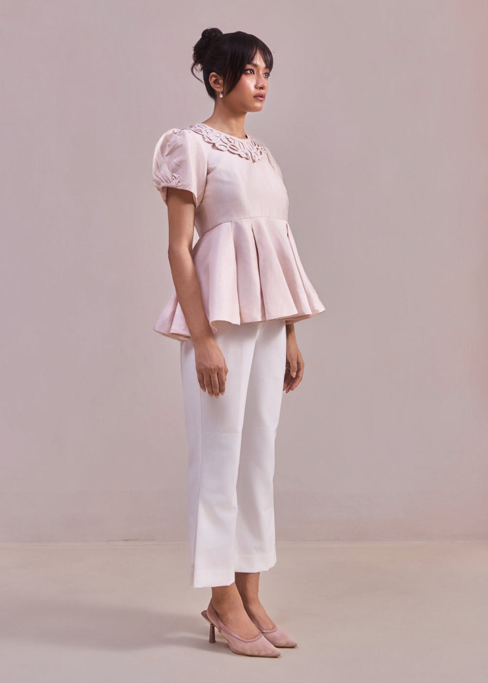Woman wearing a light pink blouse and white pants against a plain background