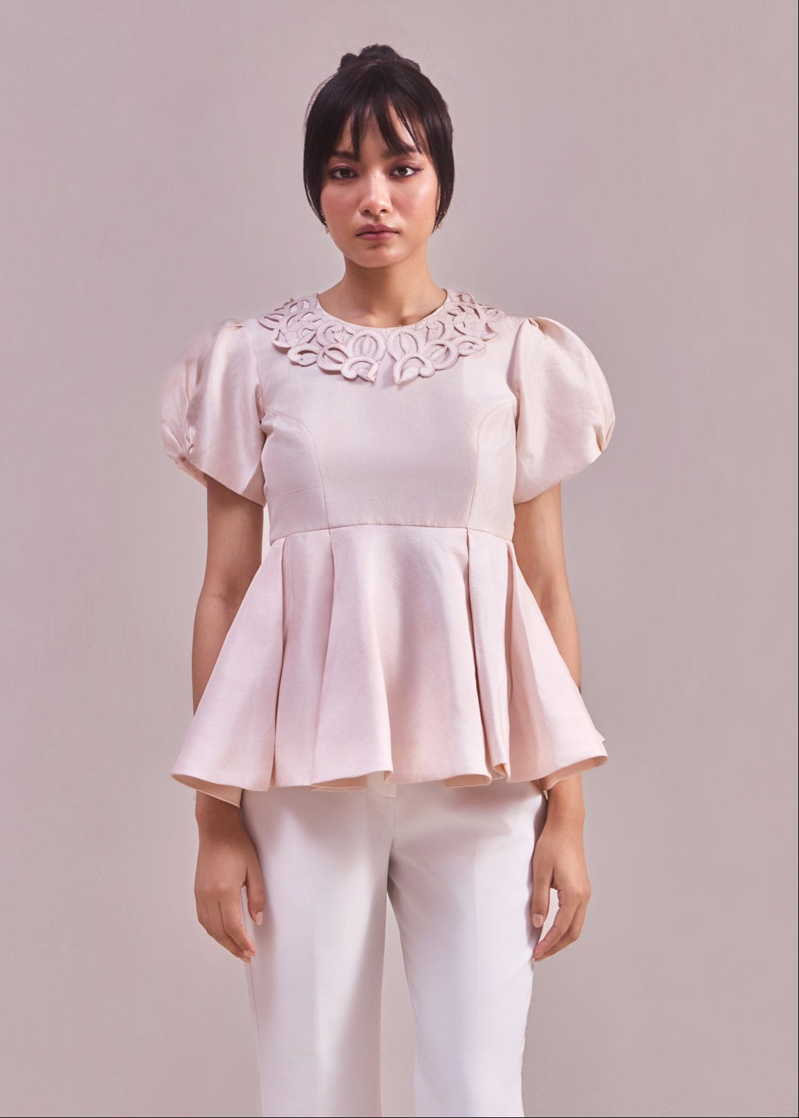 Woman wearing a light pink blouse with floral details on a plain background