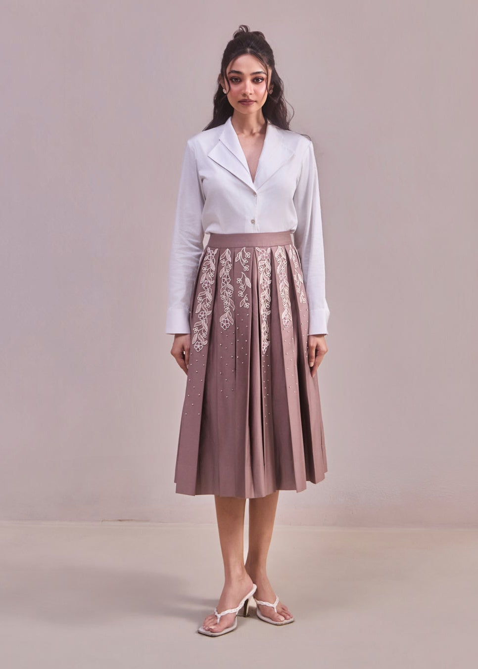 Woman wearing a white blouse and brown skirt with floral embroidery on a plain background